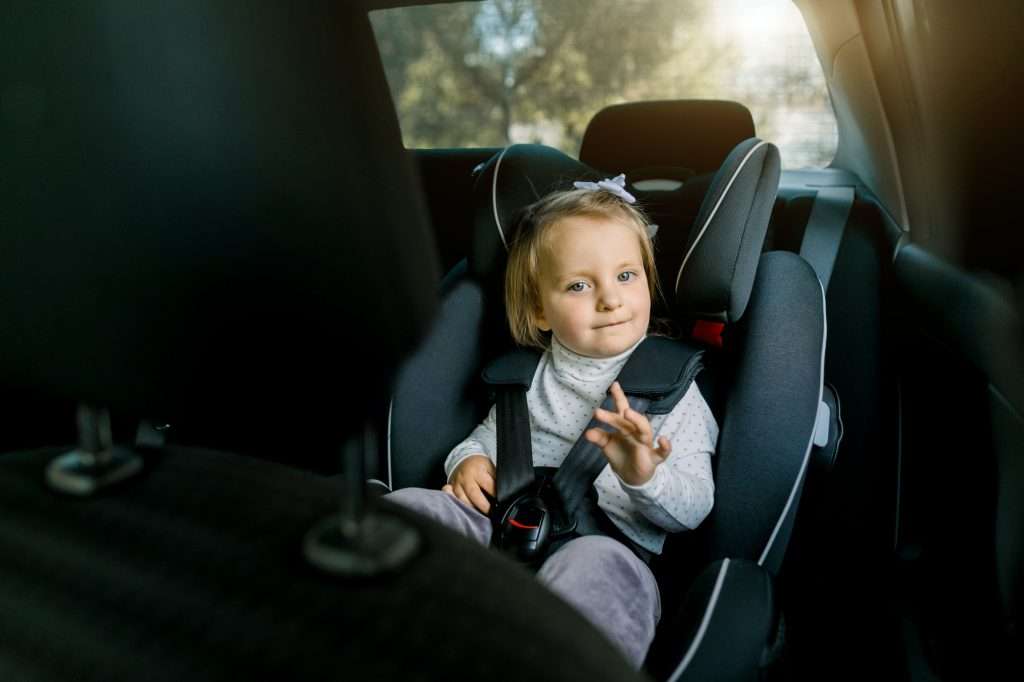 Cute Caucasian child, pretty baby girl, sitting in safety seat inside car with fastened belts