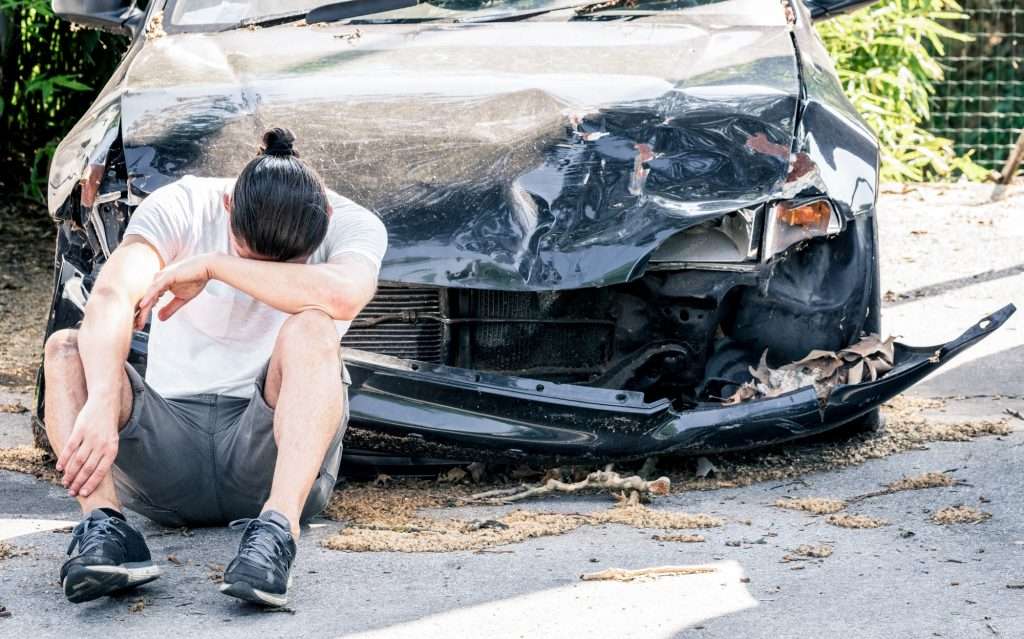 Man crying on his old damaged car after crash accident